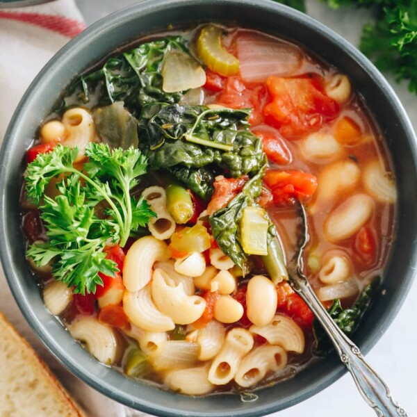 Minestrone soup recipe overhead in a blue bowl with kale and parsley on top.