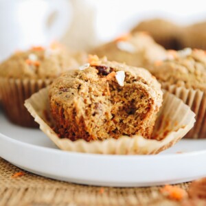 Morning glory muffins on a white platter. The muffin at the forefront has a bite taken out of it.