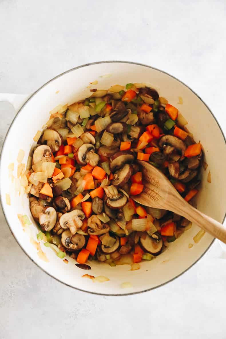 mushrooms, carrots, celery, onion and garlic cooking in a large white dutch oven.