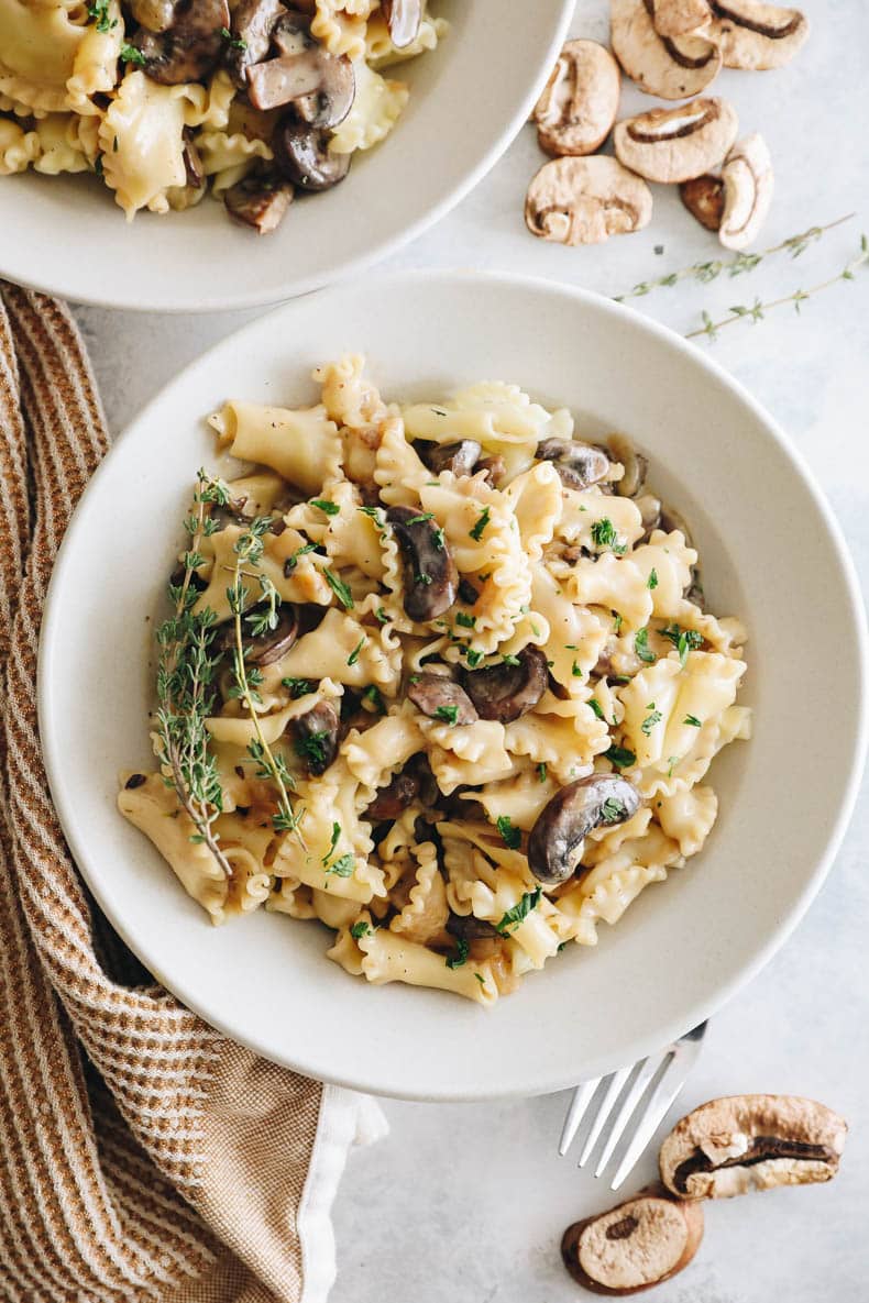 Overhead image of vegan mushroom stroganoff in a white bowl topped with creamy stroganoff sauce and parsley.