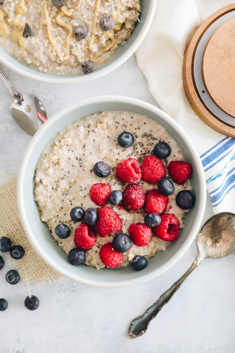 overhead photograph of overnight steel cut oats in two bowls. One bowl is topped with raspberries, blueberries and chia seeds. The other bowl is topped with chocolate chips, peanut butter and coconut.