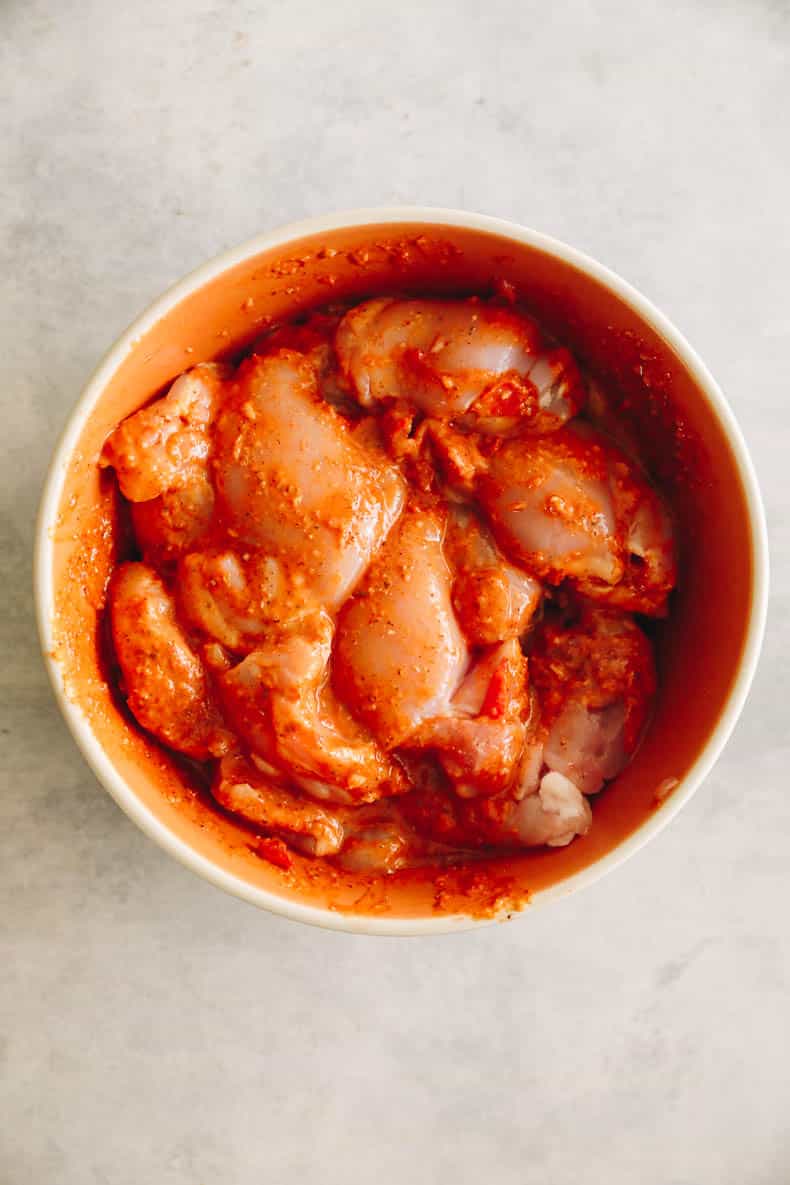 marinated peri peri chicken thighs in an orange bowl.