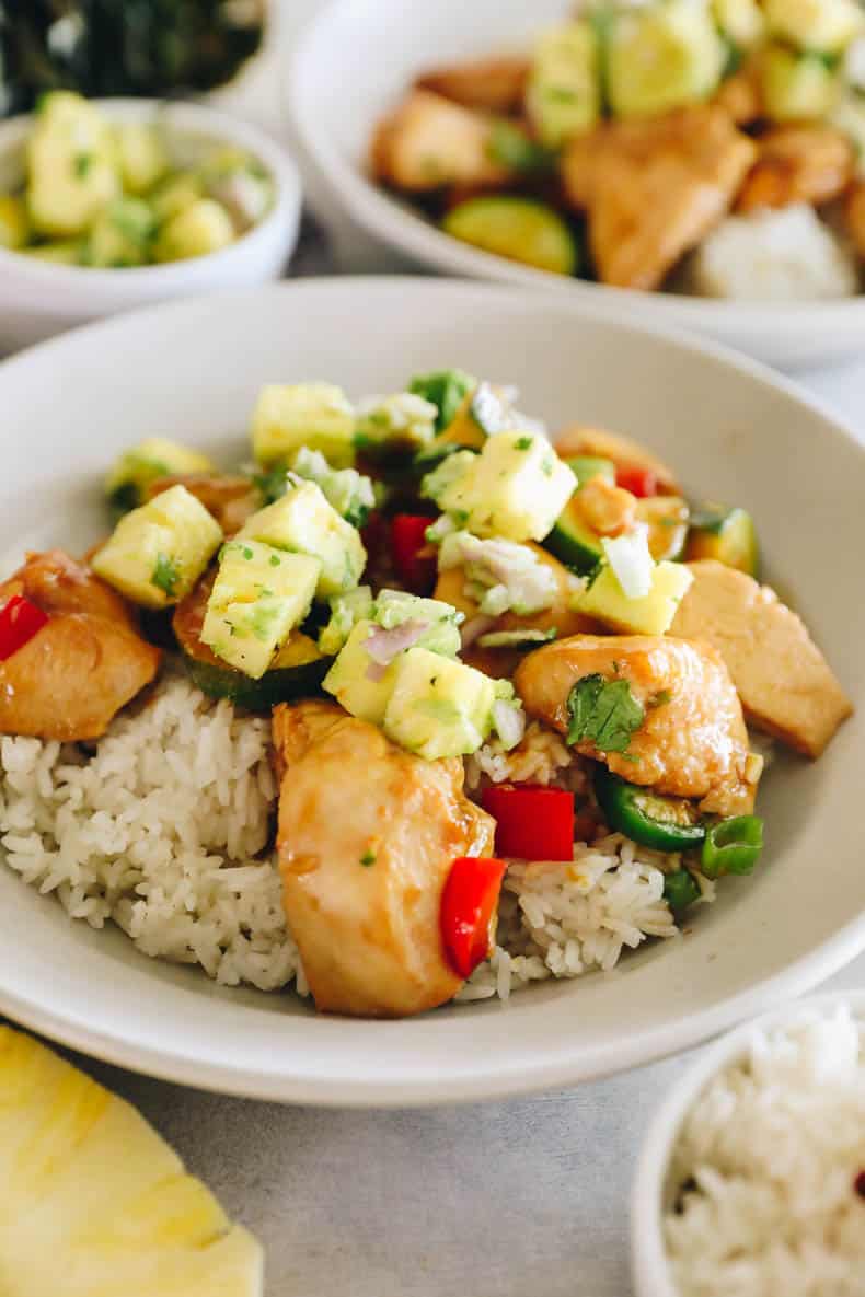 pineapple chicken with a pineapple salsa over a bed of rice in a white bowl.