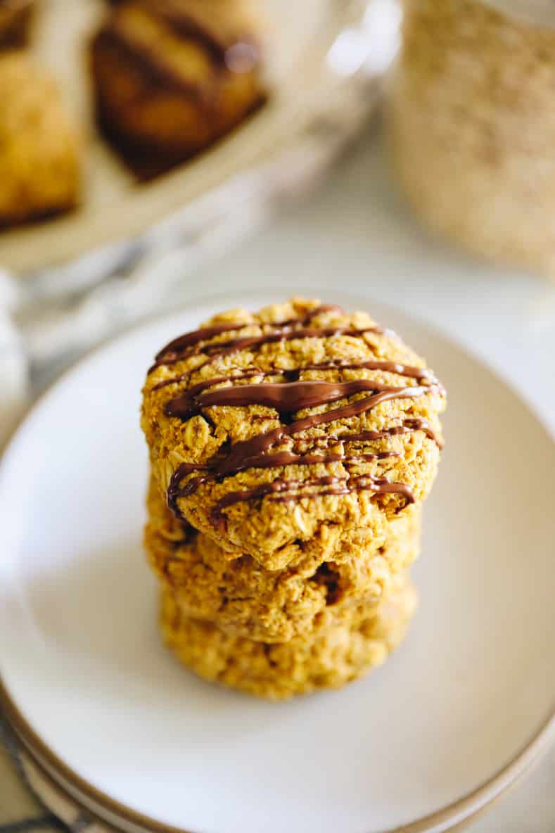 Angled shot of stacked pumpkin breakfast cookies drizzled with chocolate.