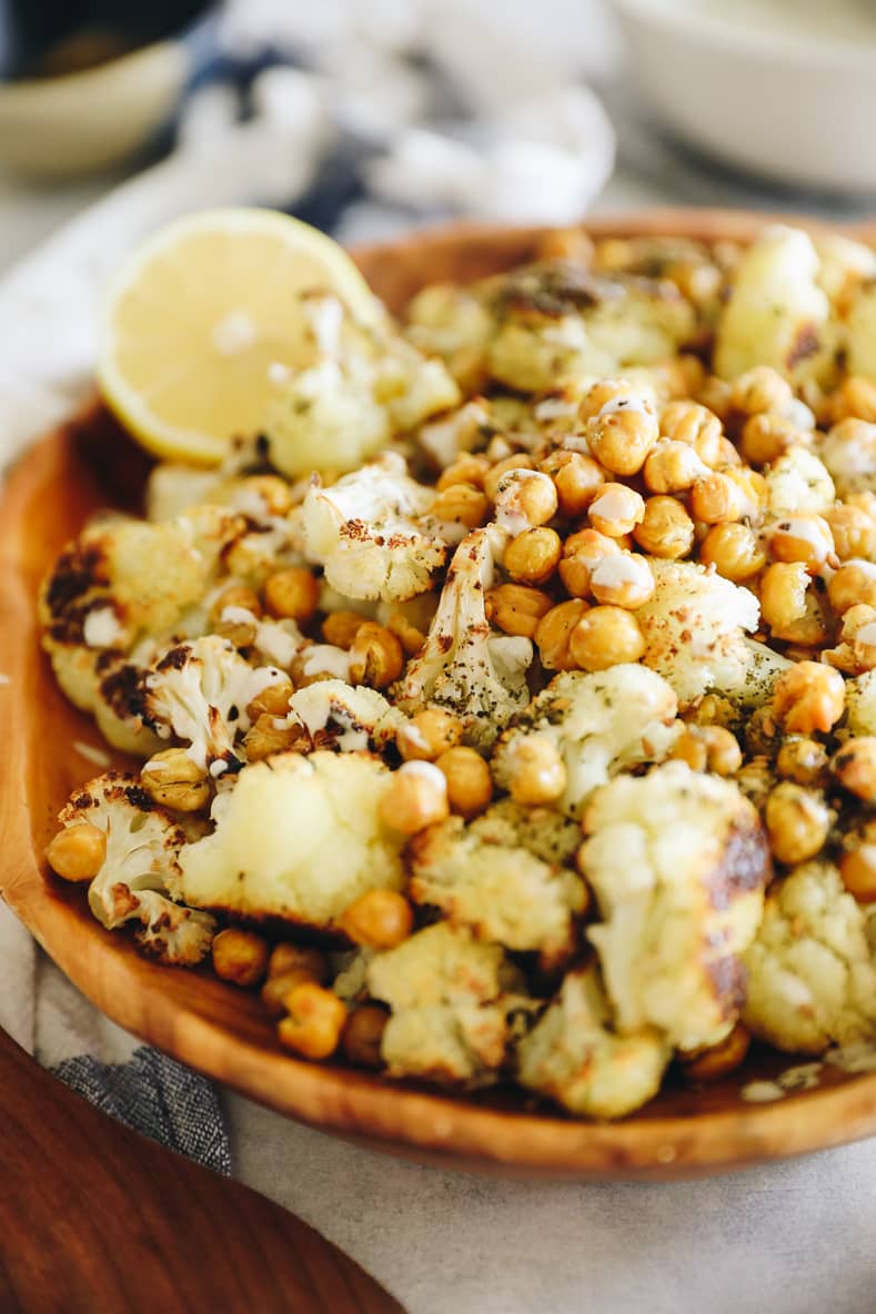 A wooden serving bowl filled with roasted cauliflower and chickpeas.