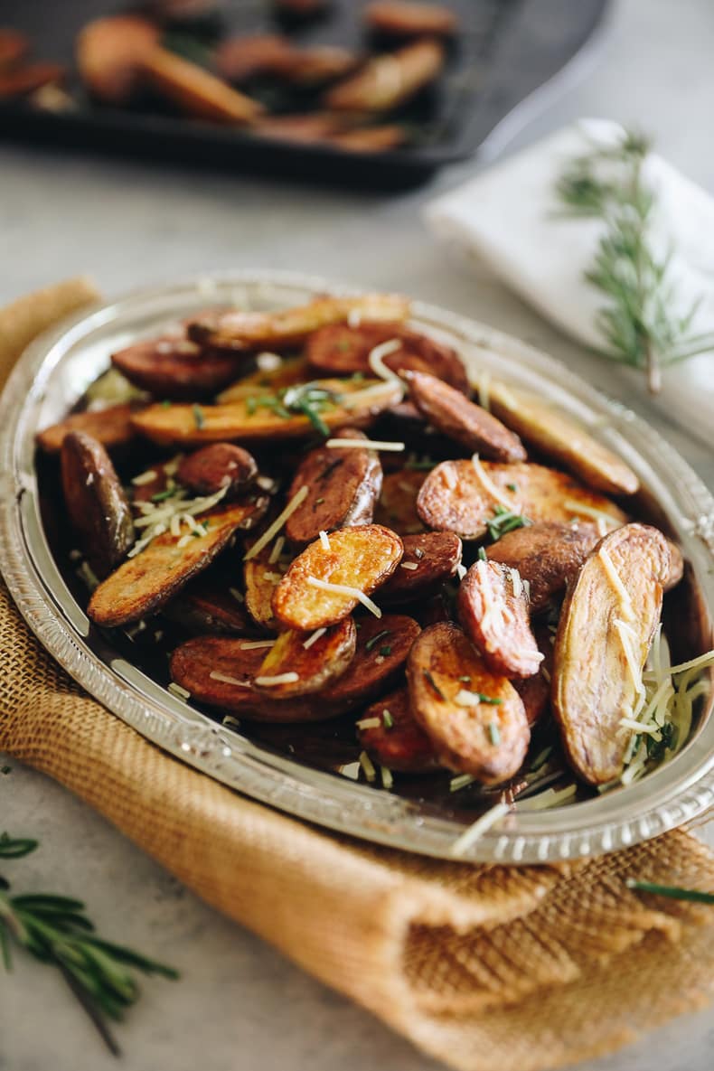 Plated dish of roasted fingerling potatoes topped with rosemary and grated parmesan cheese on a silver platter