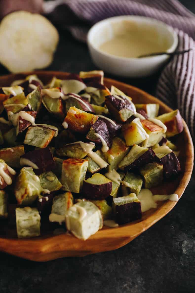 cubed and roasted japanese sweet potato topped with a miso sesame dressing in a brown shallow bowl.