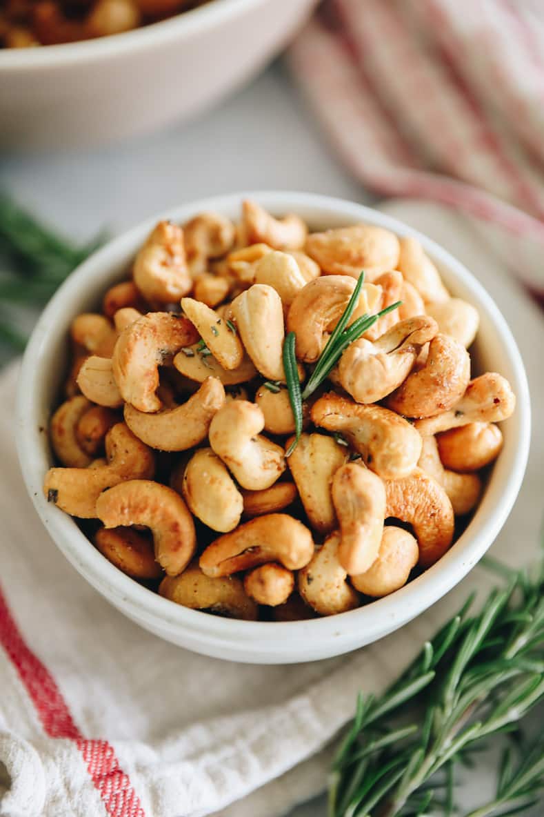 A white bowl of roasted cashews with rosemary.