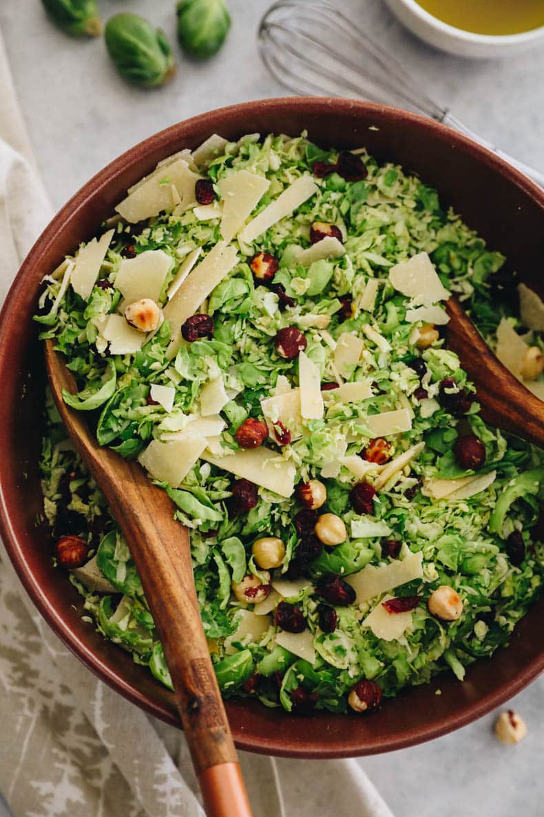 overhead image of brussel sprout salad in a brown bowl with salad tongs.