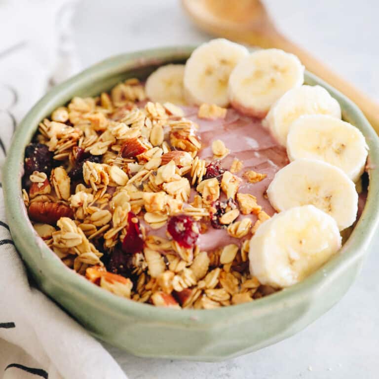 pink smoothie bowl with bananas, granola and honey.