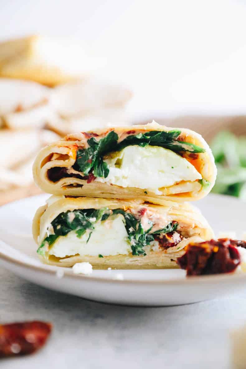 upclose image of an egg white spinach feta wrap stacked on top of each other on a white plate.