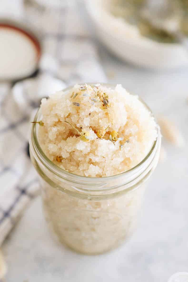 upclose image of a clear mason jar with sugar scrub and topped with chamomile and lavender.