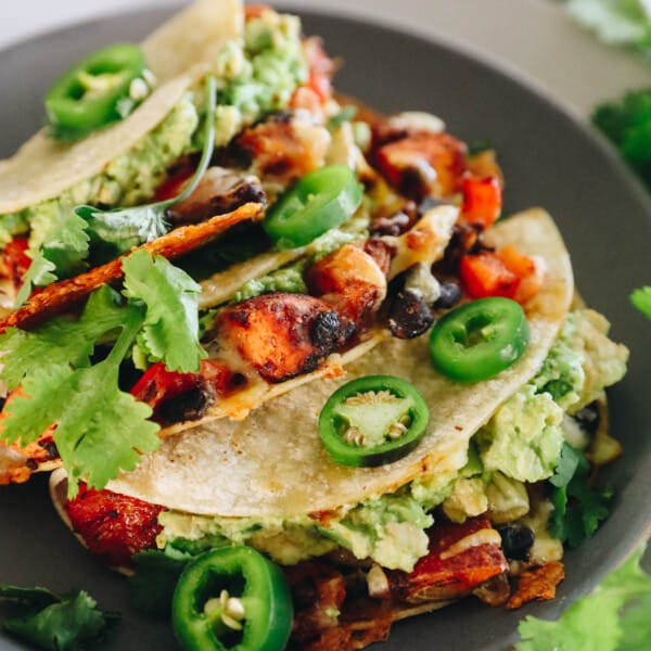 3 sweet potato and black bean tacos on a blue plate topped with jalapenos and fresh cilantro.