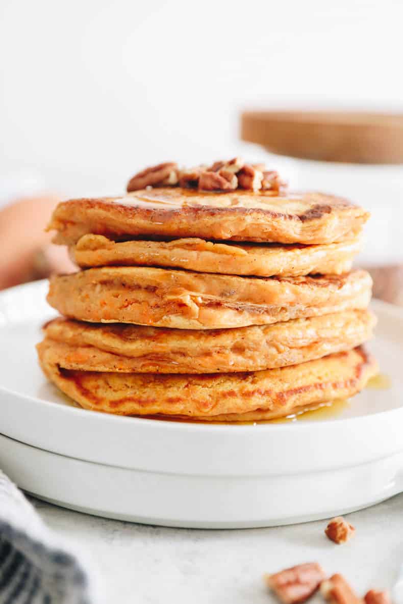 stack of sweet potato pancakes on a white plate topped with pecans.