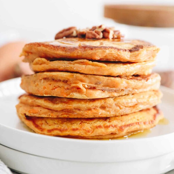 stack of sweet potato pancakes topped with crushed pecans and maple syrup.