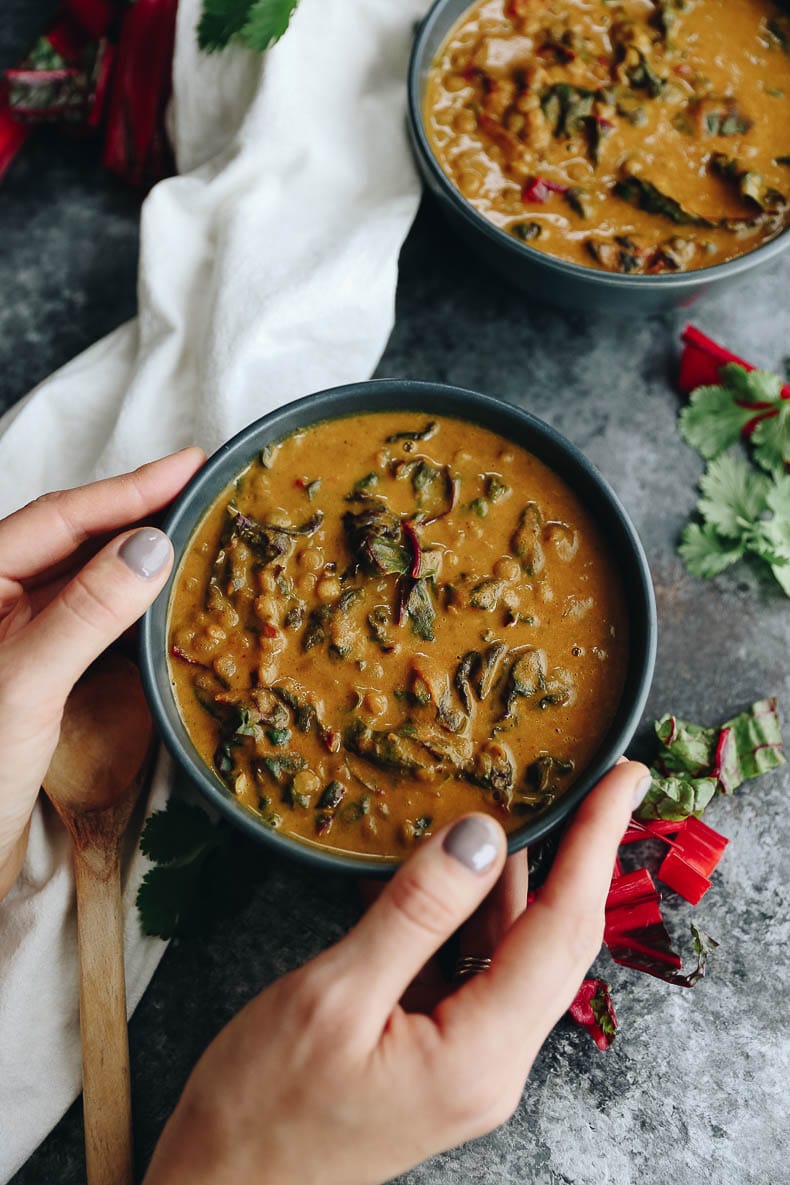 Overhead shot of Thai curry carrot lentil soup held by two hands.