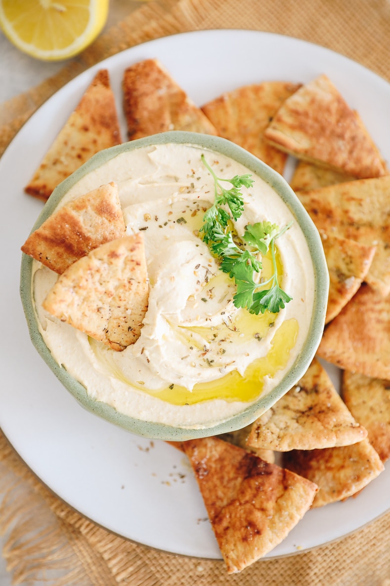 creamy homemade hummus recipe in a green bowl surrounded by pita chips