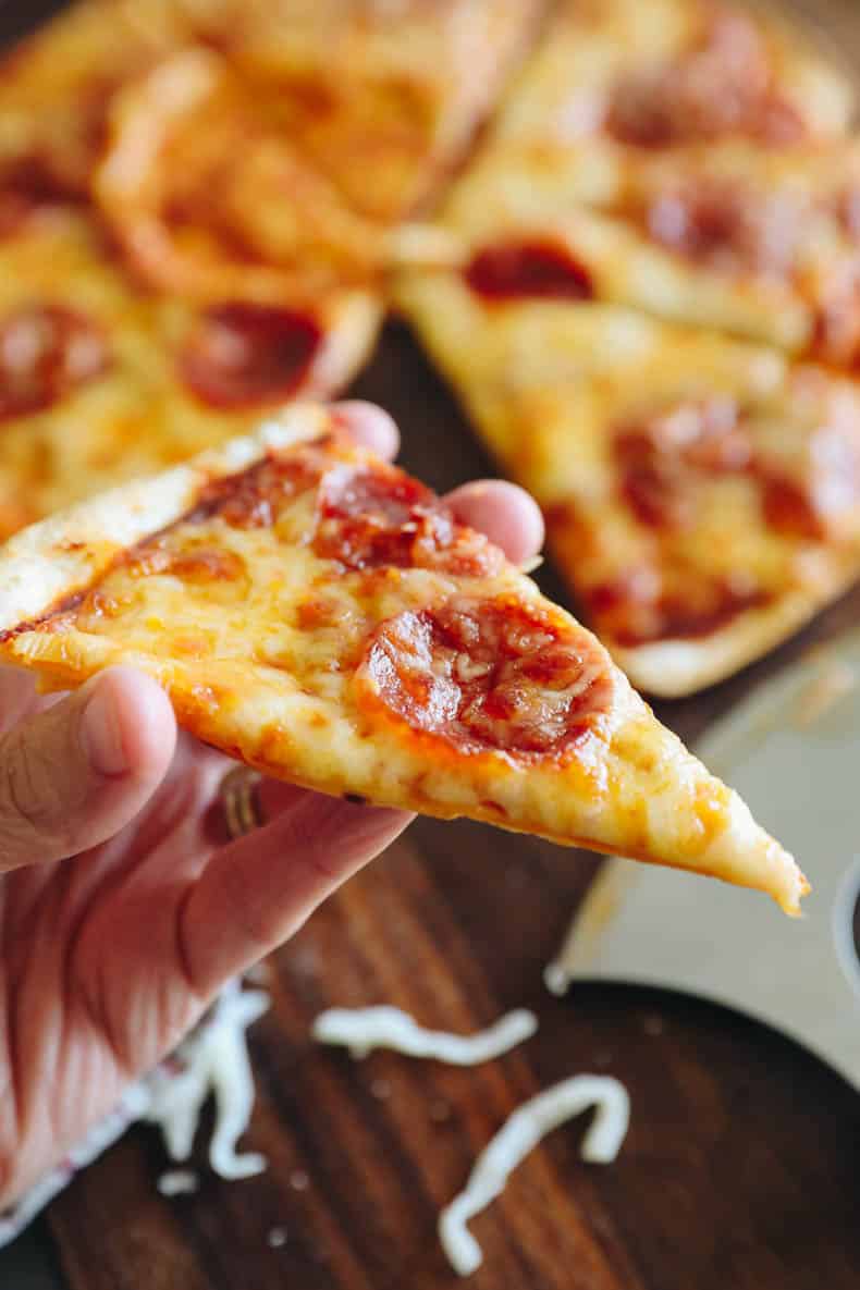 hand holding a slice of tortilla pizza