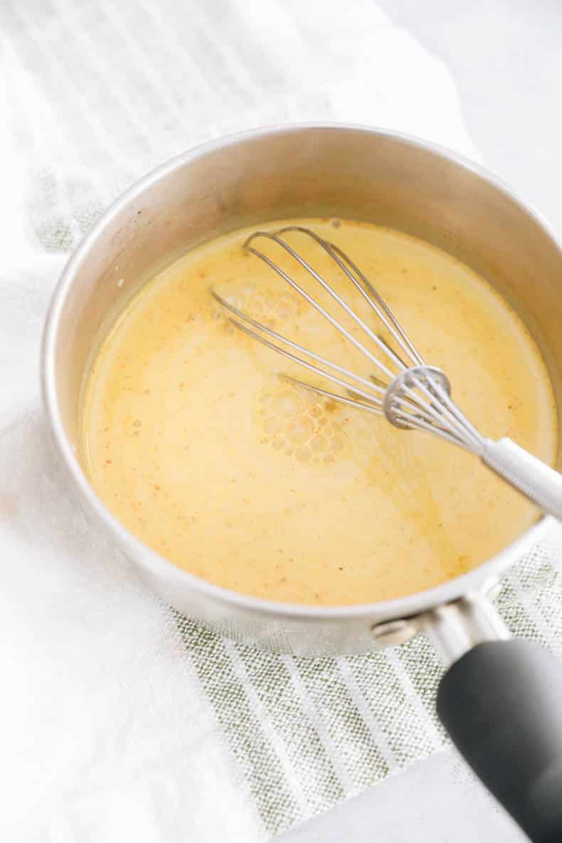 turmeric latte being cooked in a pot on the stove top with a whisk.