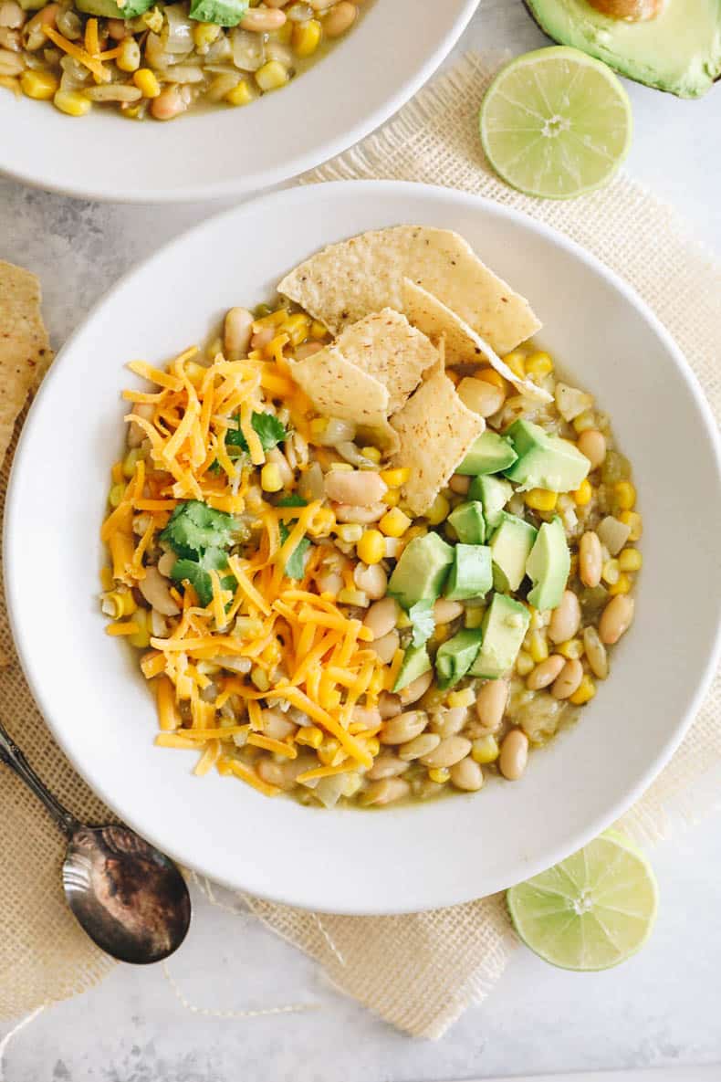 overhead image of white bean chili in a white bowl with a spoon and lime.