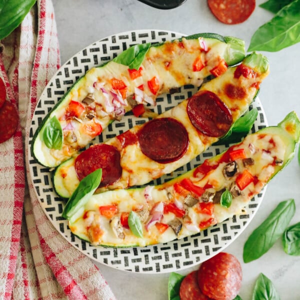 zucchini pizza boats on a black and white striped plate.